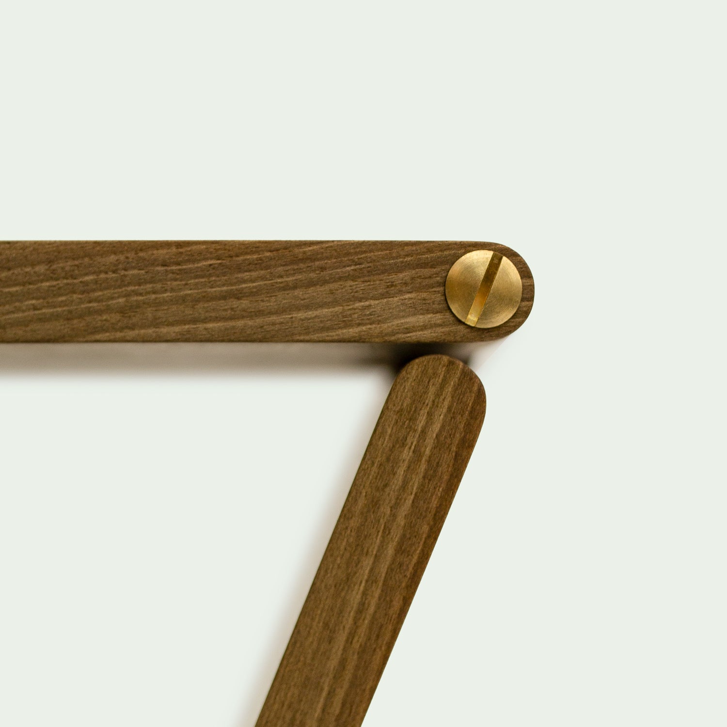 Seitliche Detailaufnahme der Messingschrauben der Gelenke vom Hocker "Holzweg", gestaltet von Marius Uminski, Variante aus Walnussholz