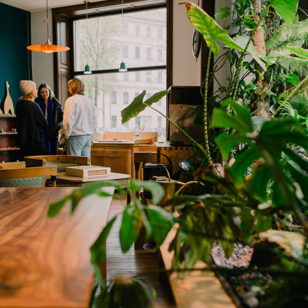 Atmosphärische Innenraumaufnahme vom mimikry, dem Designbüro in Leipzig. Der Blick wandert über den Schreibtisch "Streuobstwiese", entlang von üppingen Pflanzen, hin zu einer Gruppe von Kunden.