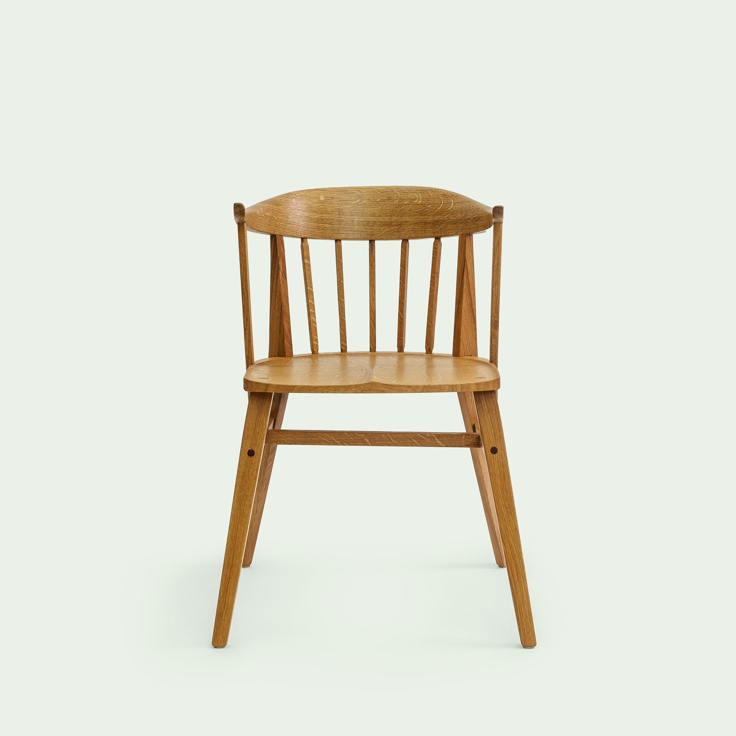 Stuhl Norderney in Vorderansicht. Die geschwungene Rückenlehne und die senkrechten Holzstreben sind deutlich zu sehen. Die Sitzfläche ist glatt und die Beine des Stuhls sind stabil und leicht nach außen geneigt. Der Stuhl besteht aus Eichenholz und ist traditionell gefertigt