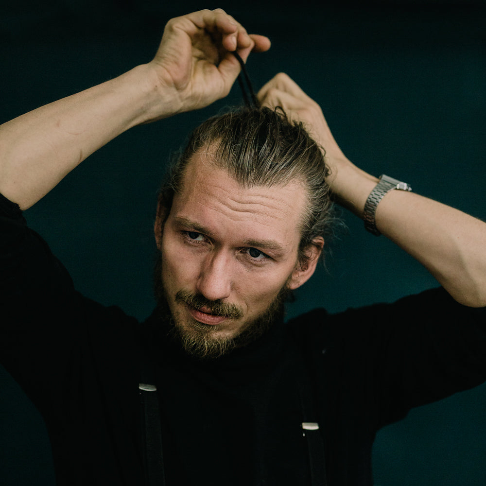 Portrait von Michael Motzek, dem Geschäftsführer von mimikry, dem Designbüro in Leipzig. Er bindet sich die langen blonden Haare zu einem Zopf und schaut zur Kamera