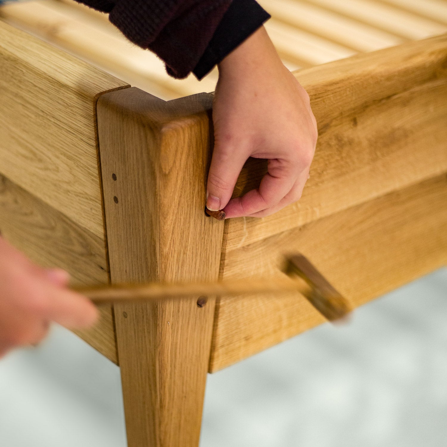Hände die die hölzernen Dübel der Schraubenlosen Verbindung des Holzbettes Norderney von mimikry befestigen indem sie die Holzdübel mit dem Hammer reintreiben.