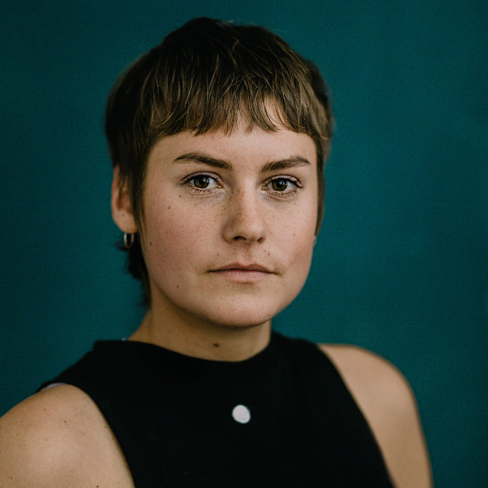 Ernstes Porträt von Ramona Rapp mit kurzem, hellbraunem Haar und einem Ohrring, die zur Seite schaut und lächelt, vor einem dunklen Hintergrund.