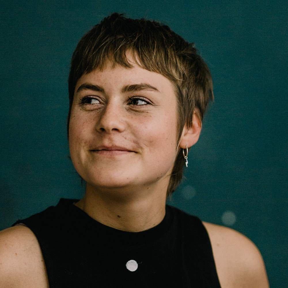 Porträt von Ramona Rapp mit kurzem, hellbraunem Haar und einem Ohrring, die zur Seite schaut und lächelt, vor einem dunklen Hintergrund.