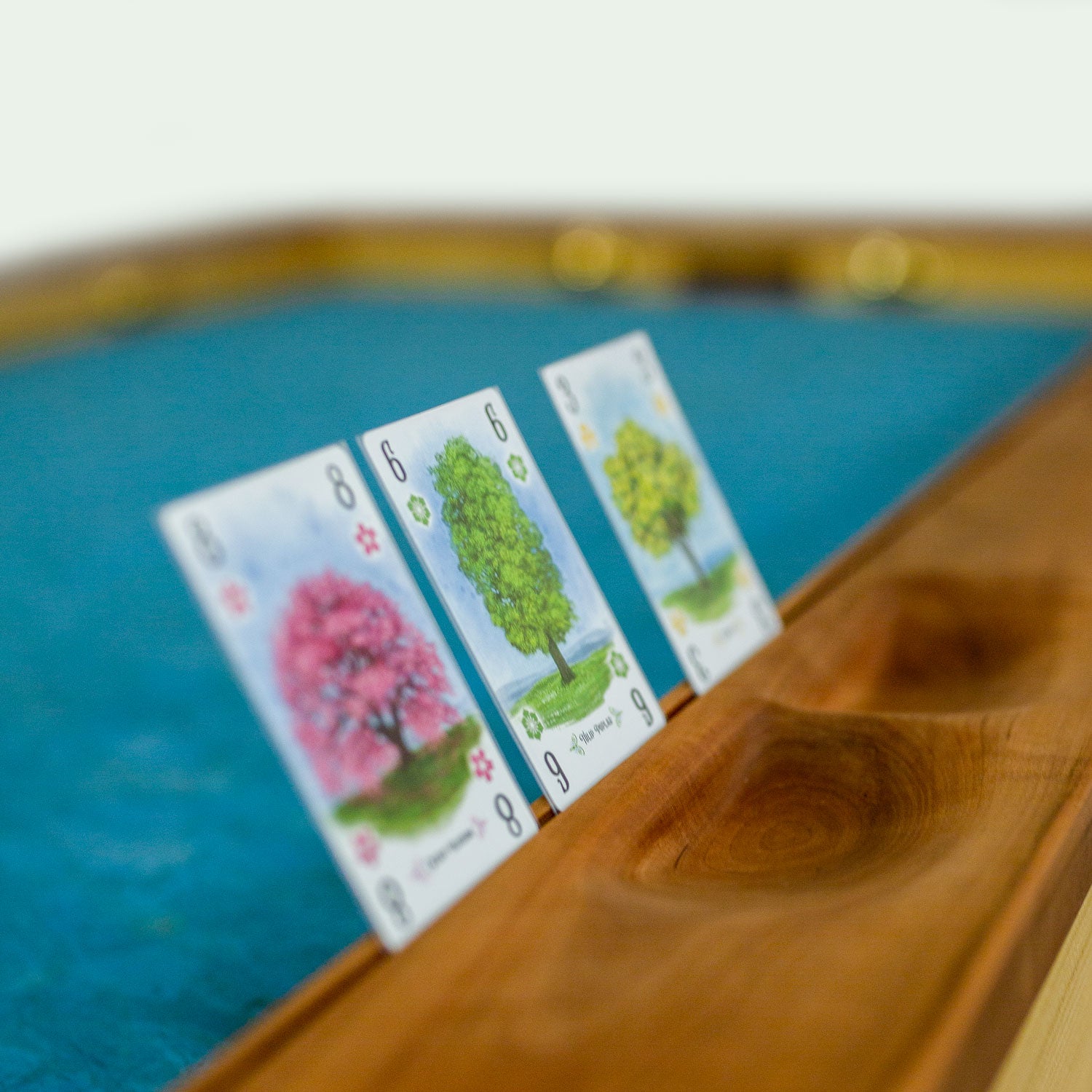 Nahaufnahme von Drei Spielekarten in der Kartenaufnahme des Spieletisches Corbin. Außerdem sieht man von hand gefertigte Mulden für die Würfel und Spielsteine.