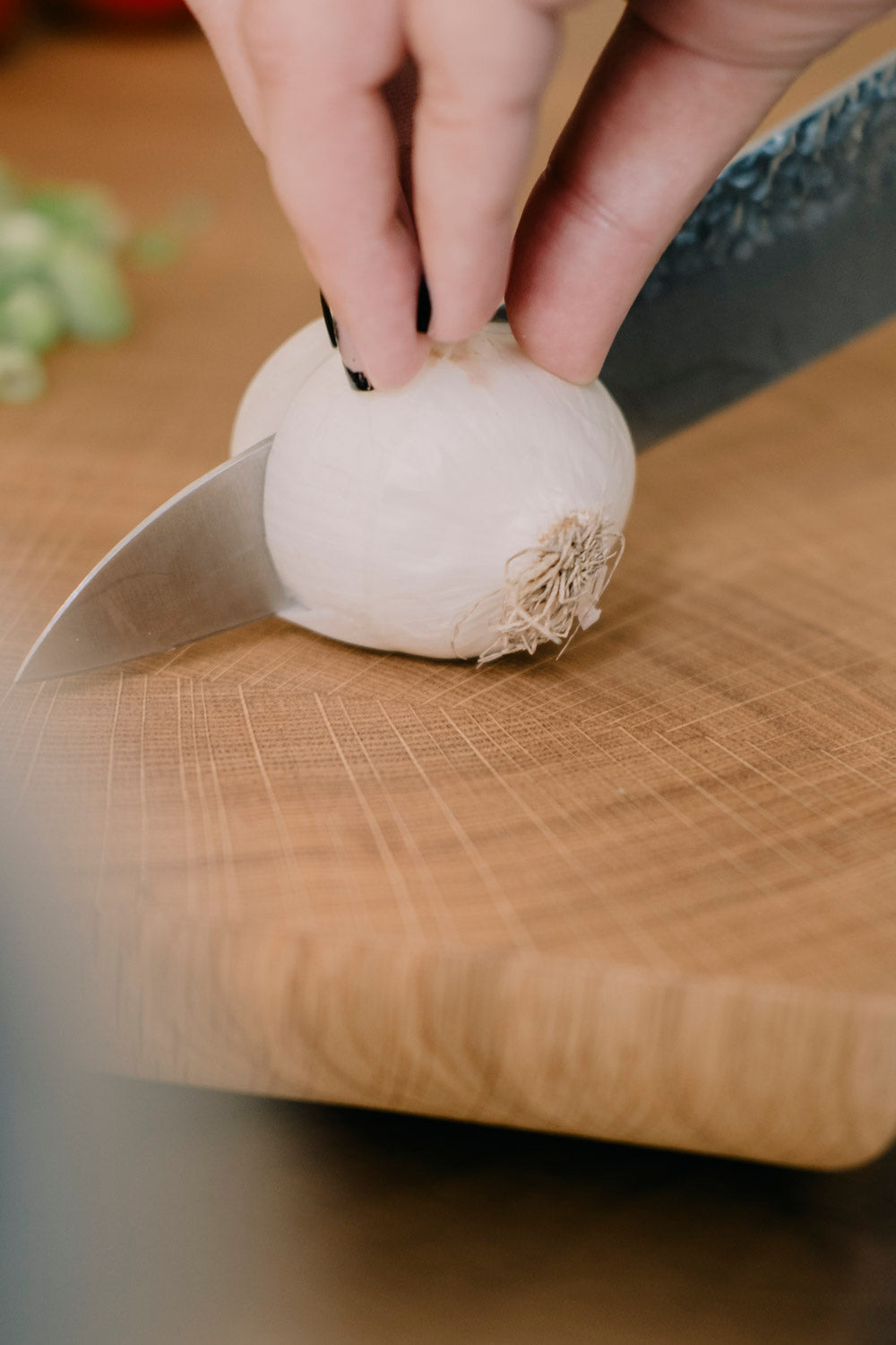 Nahaufnahme einer Hand, die auf einem Hirnholz Schneidebrett aus Eiche eine Zwiebel schneidet