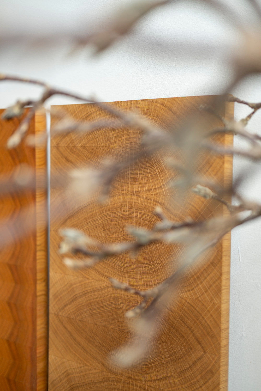 Blick durch einen Strauch trockener Blumen auf ein Hirnholz Schneidebrett aus Eiche, dass an der Wand einer Galerie lehnt
