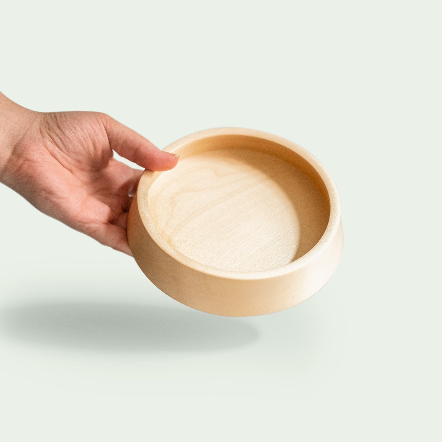 Hand hält eine handgefertigte kleine Schale aus Ahornholz mit glatter Oberfläche und natürlicher Maserung.