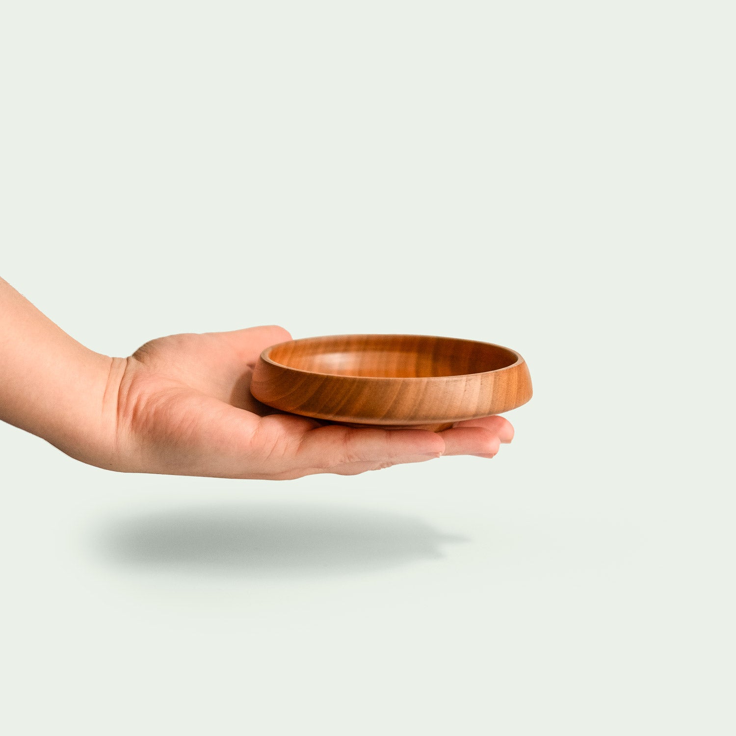 Hand hält eine handgefertigte sehr kleine Schale aus Kirschholz mit feiner Holzmaserung.