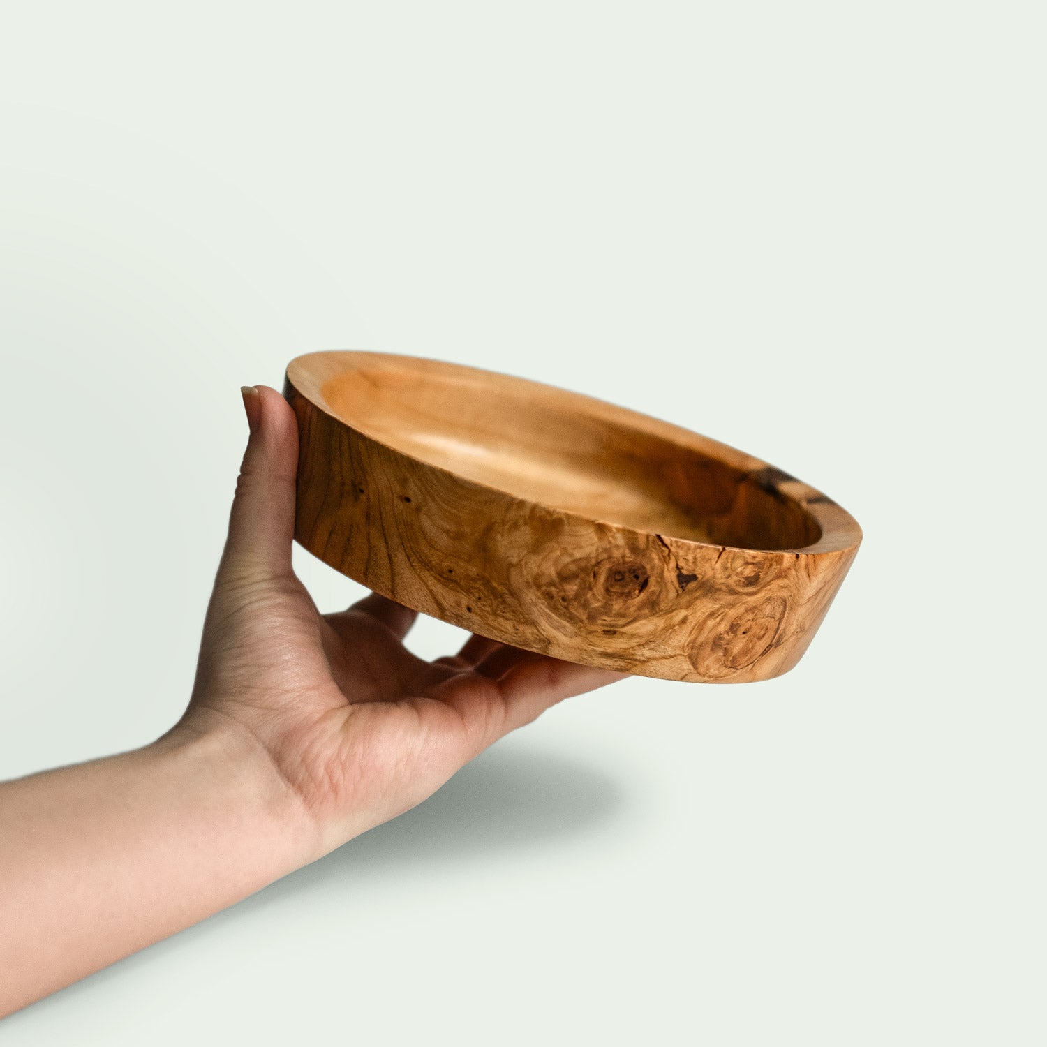 Hand hält eine handgefertigte Holzschale aus verwurzeltem Kirschholz mit einzigartiger Maserung.