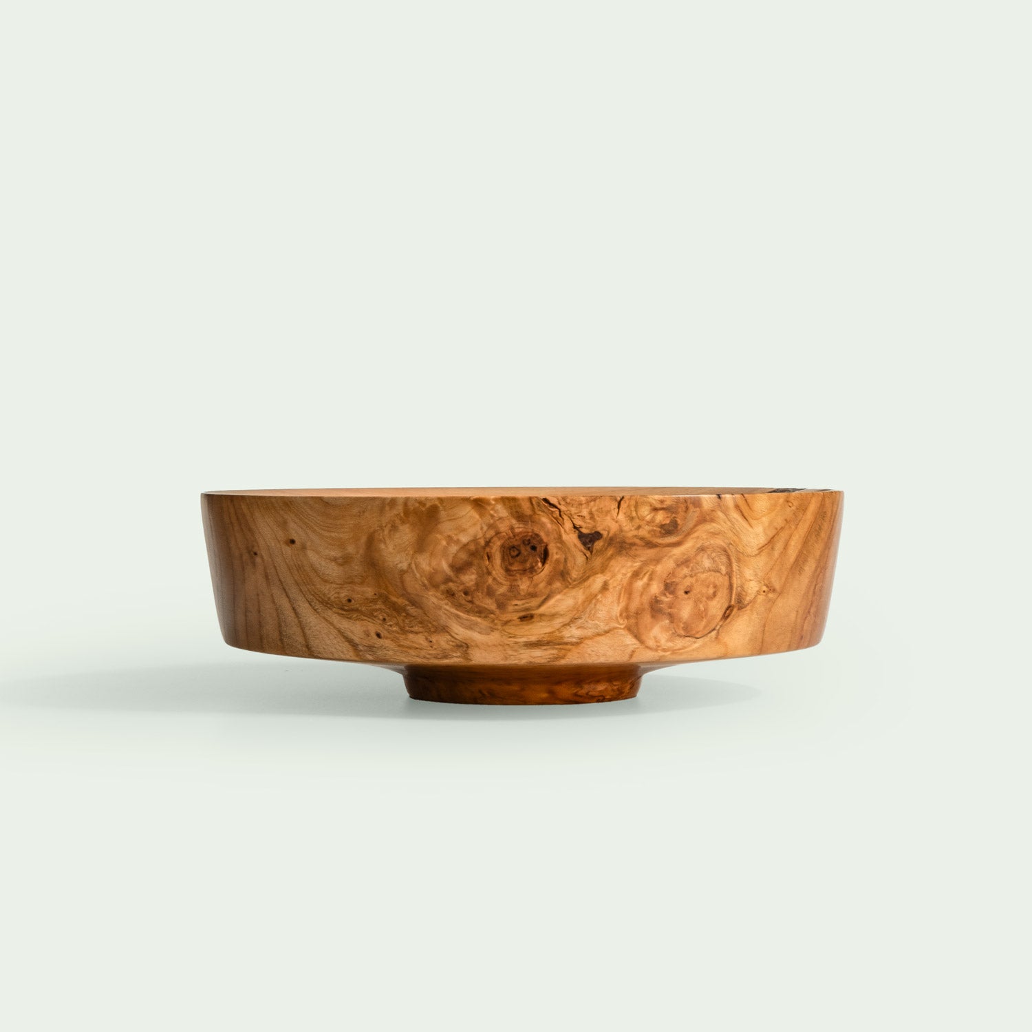 Eine handgefertigte Holzschale aus verwurzeltem Kirschholz mit einzigartiger Maserung steht in einem weißen Raum.