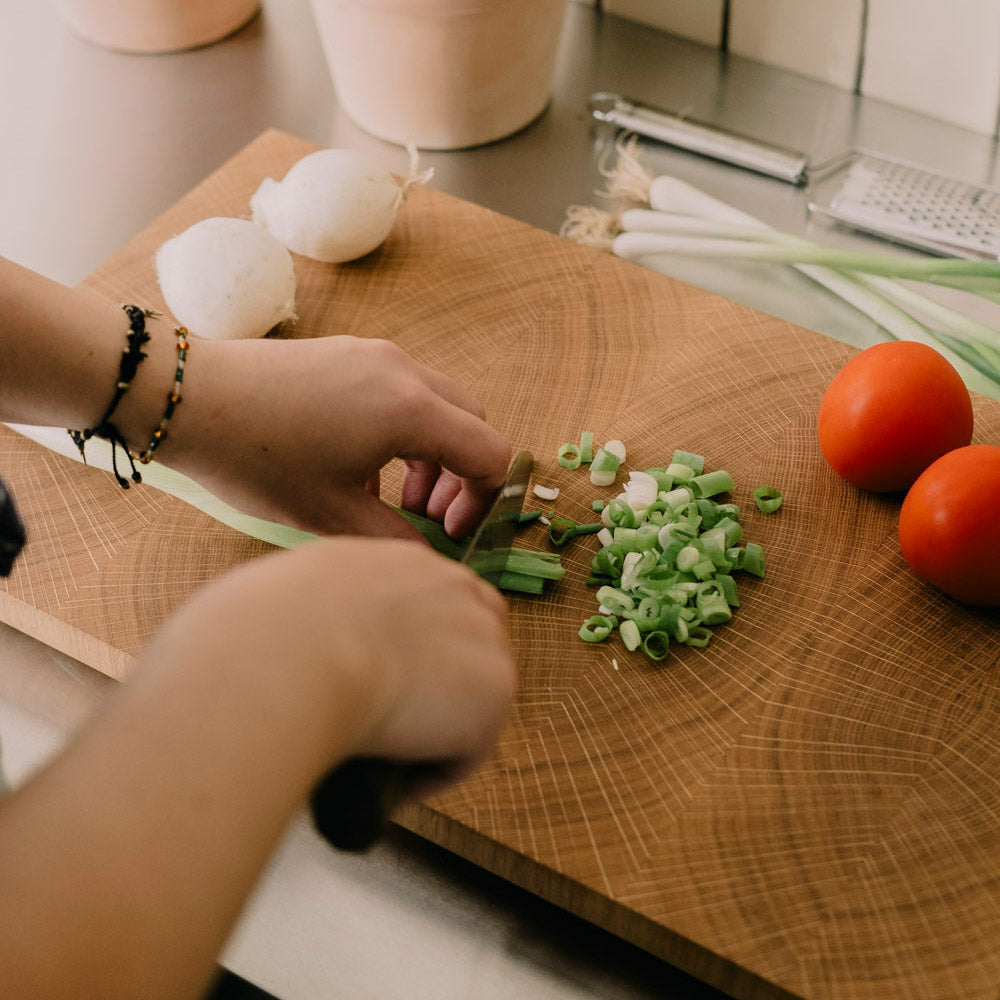 Hirnholz Schneidebrett aus Eiche, Blick über die Hände einer Person die auf dem Hirnholz Schneidebrett Lauch schneidet.