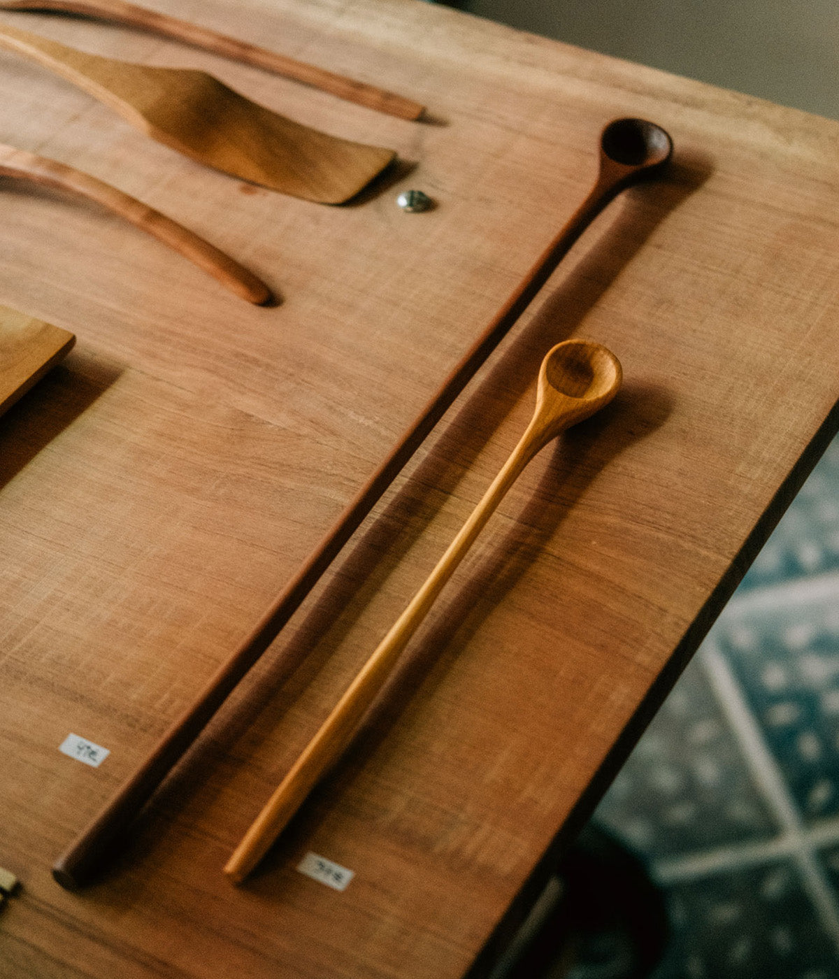 Detailaufnahme zweier handgefertigter Holzlöffel der Marke mimikry. Sie liegen nebeneinander auf einem glänzenden Kirschholztisch.