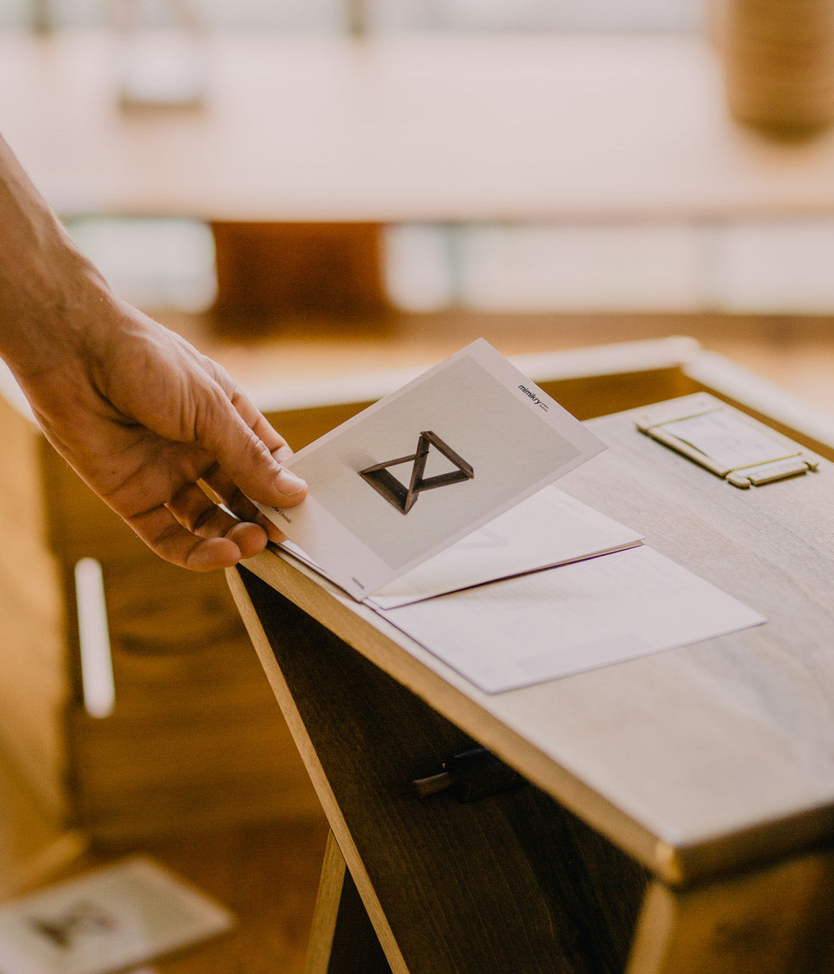 Nahaufnahme einer Hand, die die Produktkarte des Holzweg Hocker aufnimmt.