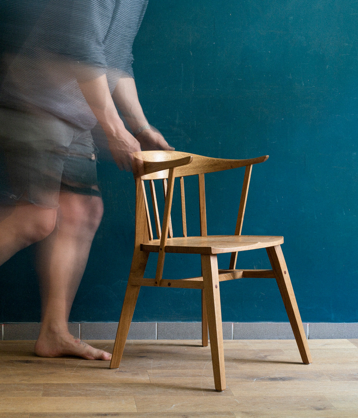 Eine schemenhafte Gestalt schiebt den Norderney Stuhl der Marke mimikry durch einen lichtdurchfluteten Raum. Durch die lange Belichtungszeit ider die Person verschwommen, der Stuhl aber scharf abgebildet.