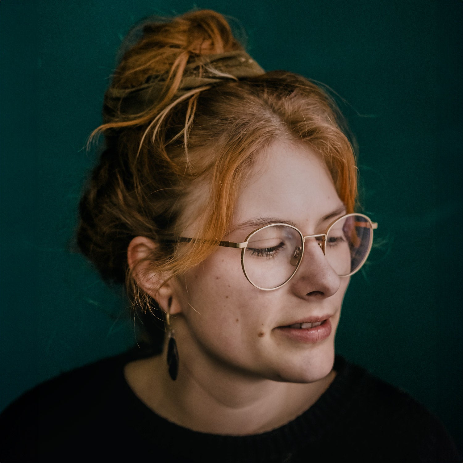 Porträt von Pauline Gutschow, mit rotblonden Haaren, Brille und Ohrringen, die nach rechts blickt und lächelt.