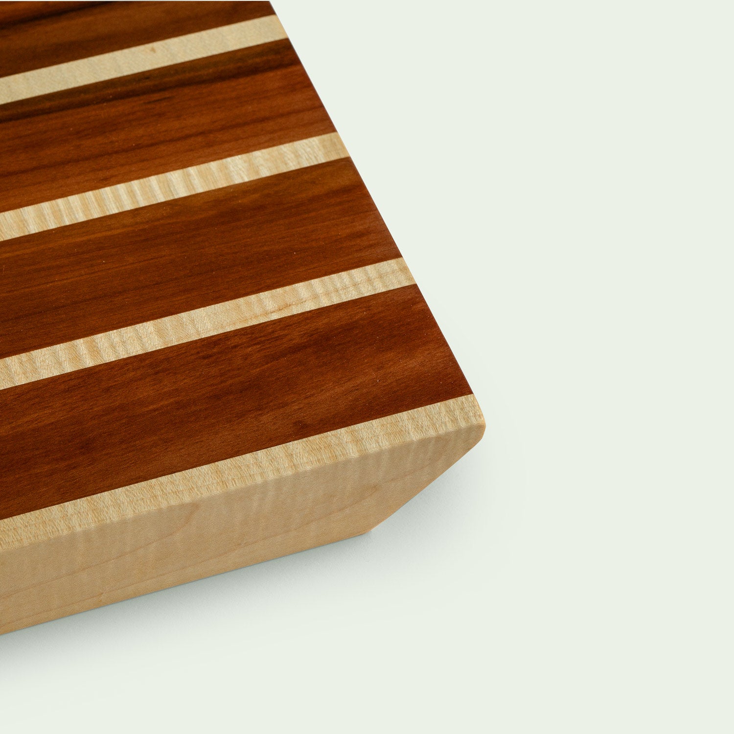 Detailansicht eines Holzschneidebretts mit gestreiftem Muster aus Ahorn und Elsbeere, Nahaufnahme einer Ecke.