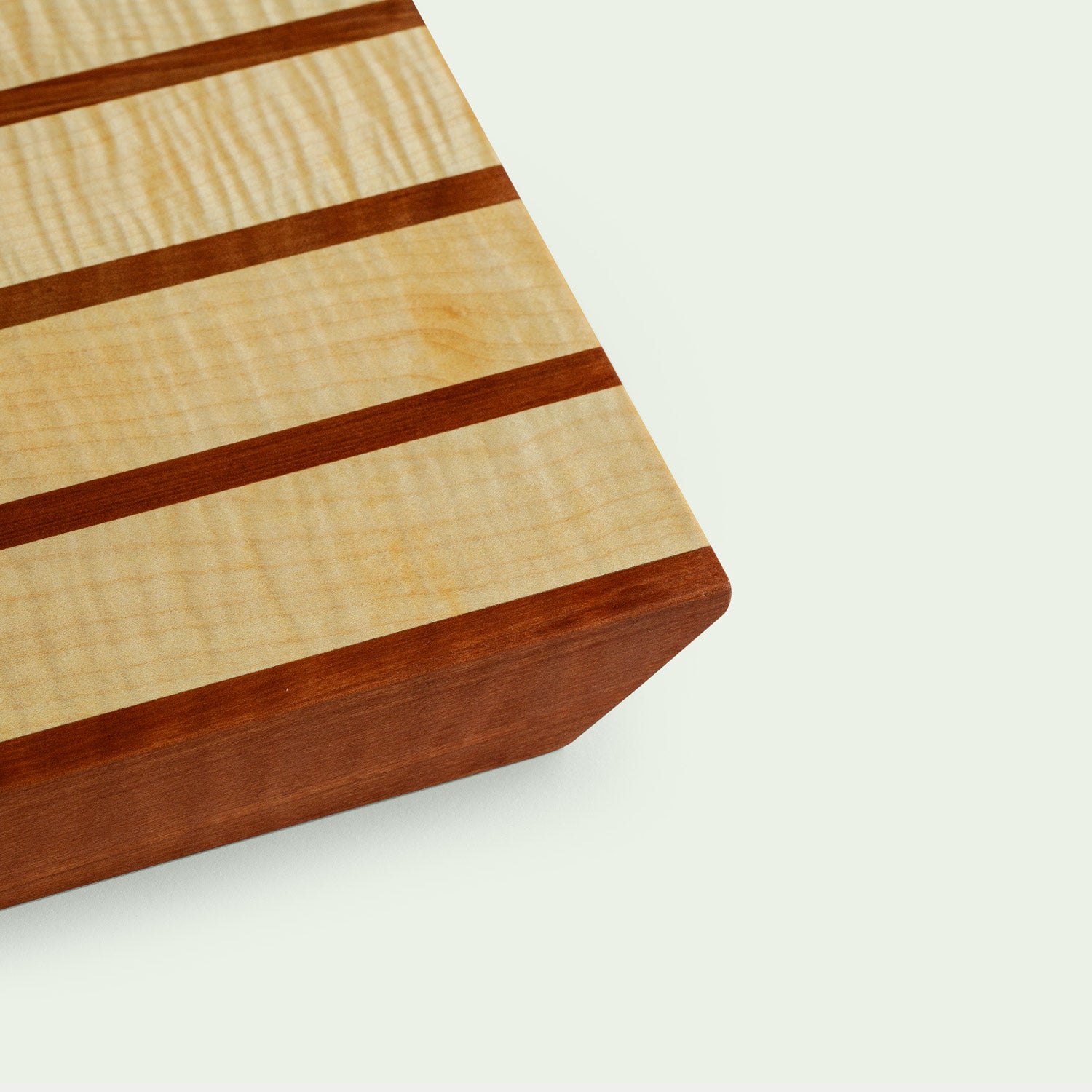 Detailansicht eines Holzschneidebretts mit gestreiftem Muster aus Ahorn und Elsbeere, Nahaufnahme einer Ecke.