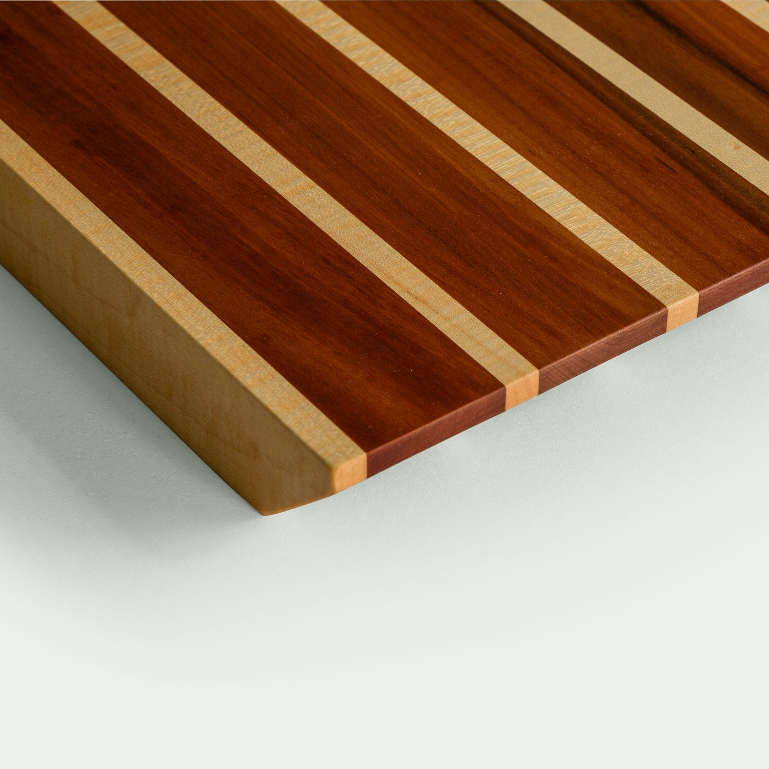 Detailansicht eines Holzschneidebretts aus Ahorn und Elsbeere mit gestreiftem Muster, dreieckiger Schnitt.