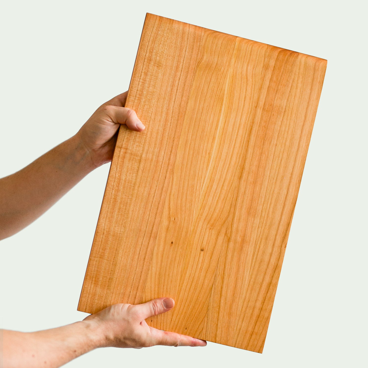 Schneidebrett Holz Groß Kirsche ohne saftrille gehalten von zwei händen vor einem hellen hintergrund, Hergestellt von der Tischlerei mimikry in Leipzig
