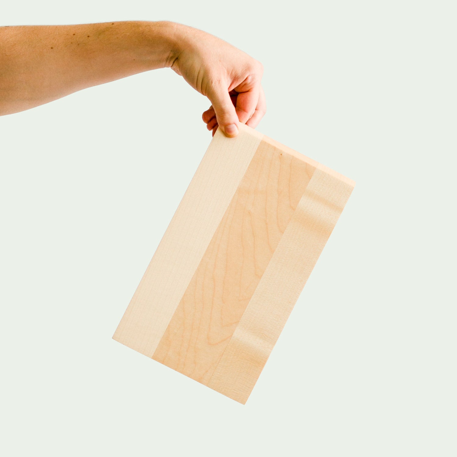 Hochwertiges Frühstückbrett aus Ahorn Holz wird von einer Hand quer ins Bild gehalten