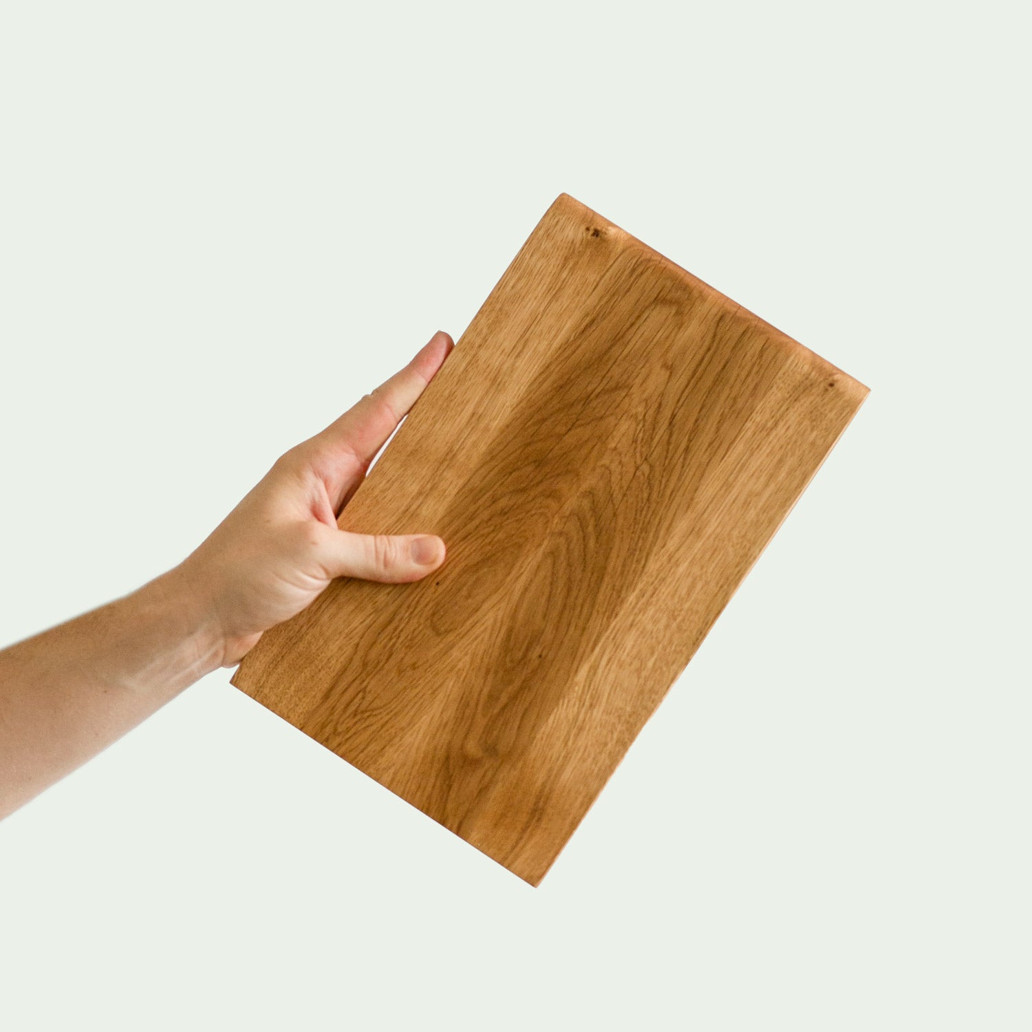 Hochwertiges Frühstückbrett aus Eiche Holz wird von einer Hand quer ins Bild gehalten