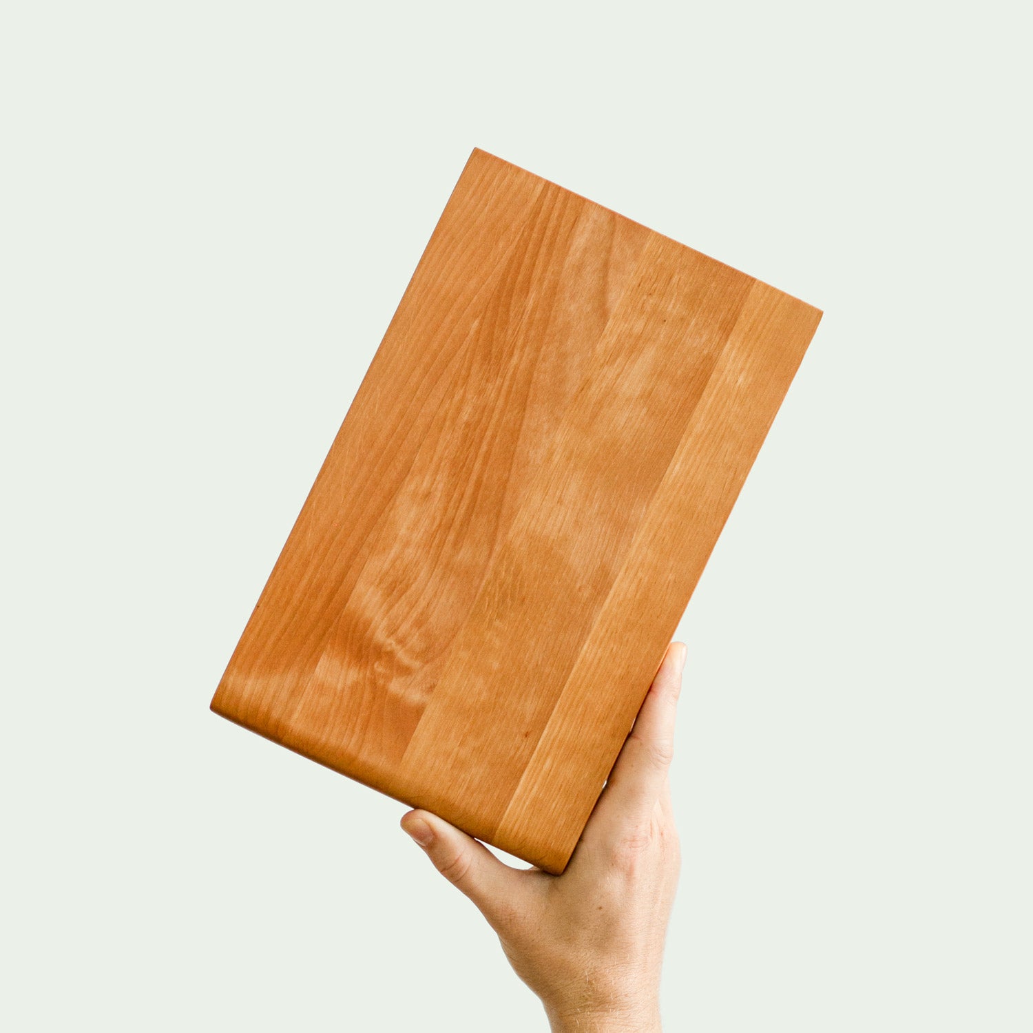 Hochwertiges Frühstückbrett aus Erle Holz wird von einer Hand quer ins Bild gehalten