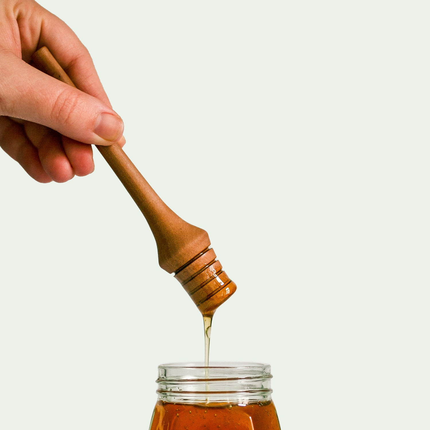 Ein Honiglöffel aus Holz, der Serie "Elsbeere" wird in der Hand gehalten, während Honig aus einem Glas aufgenommen wird, was die Handhabung und Funktionalität demonstriert.