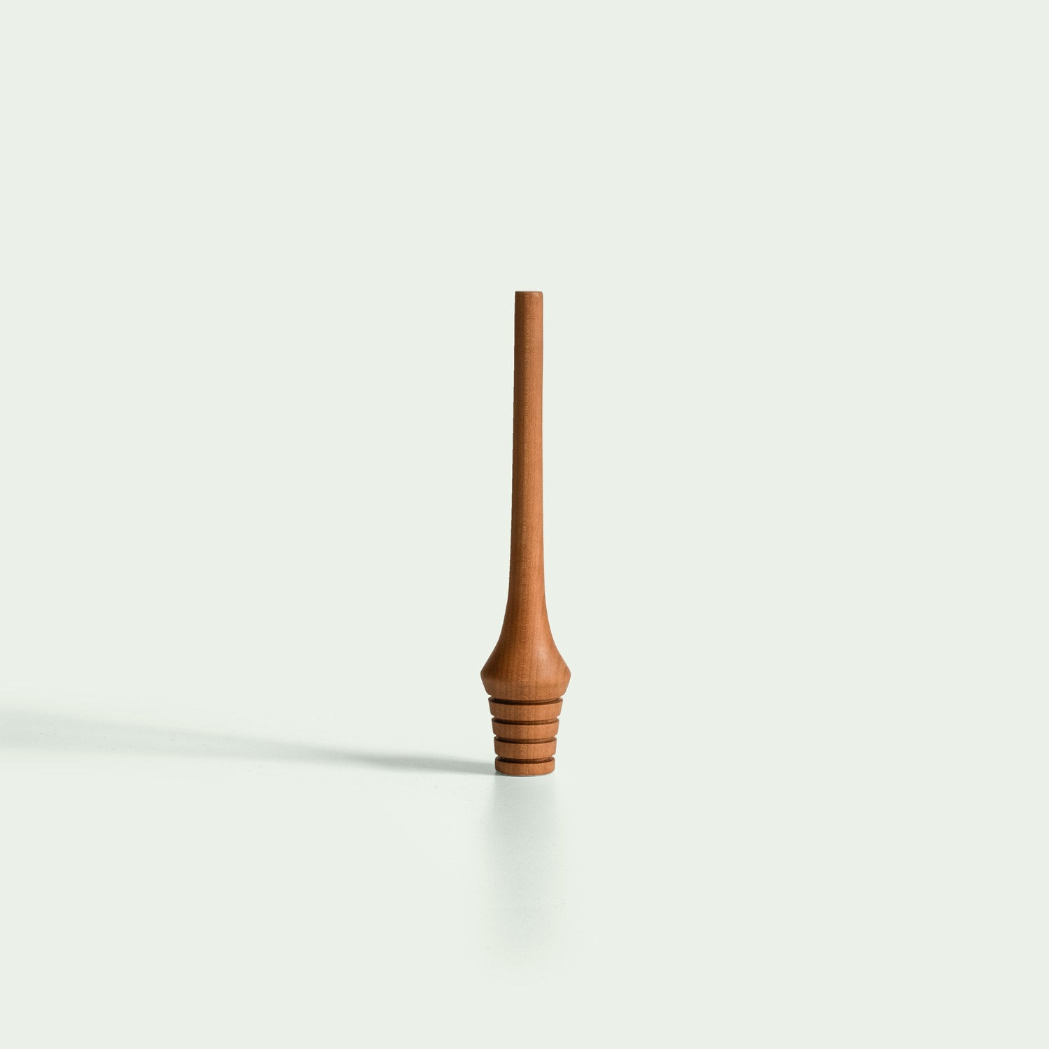 Ein Honiglöffel aus Holz, der aufrecht steht. Der Löffel hat einen langen, schlanken Griff und am unteren Ende befinden sich mehrere Einkerbungen für das Aufnehmen von Honig. Die Oberfläche des Löffels ist glatt und poliert.