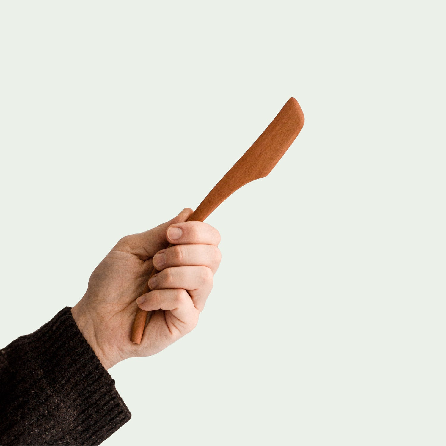 Hand hält handgefertigtes Buttermesser aus Elsbeere mit ergonomischem Griff und glatter, leicht gebogener Klinge, nachhaltig produziert.