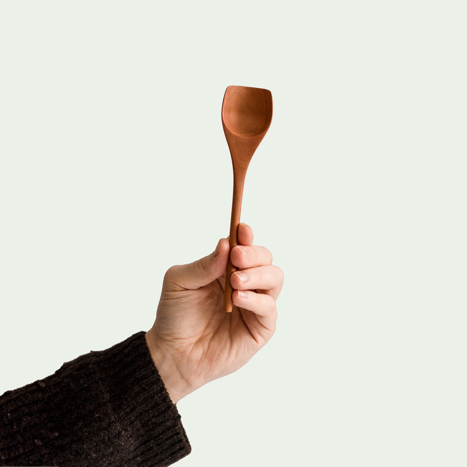 Hand hält handgefertigten Esslöffel aus Elsbeere, nachhaltig produziert. minimalistisches Design