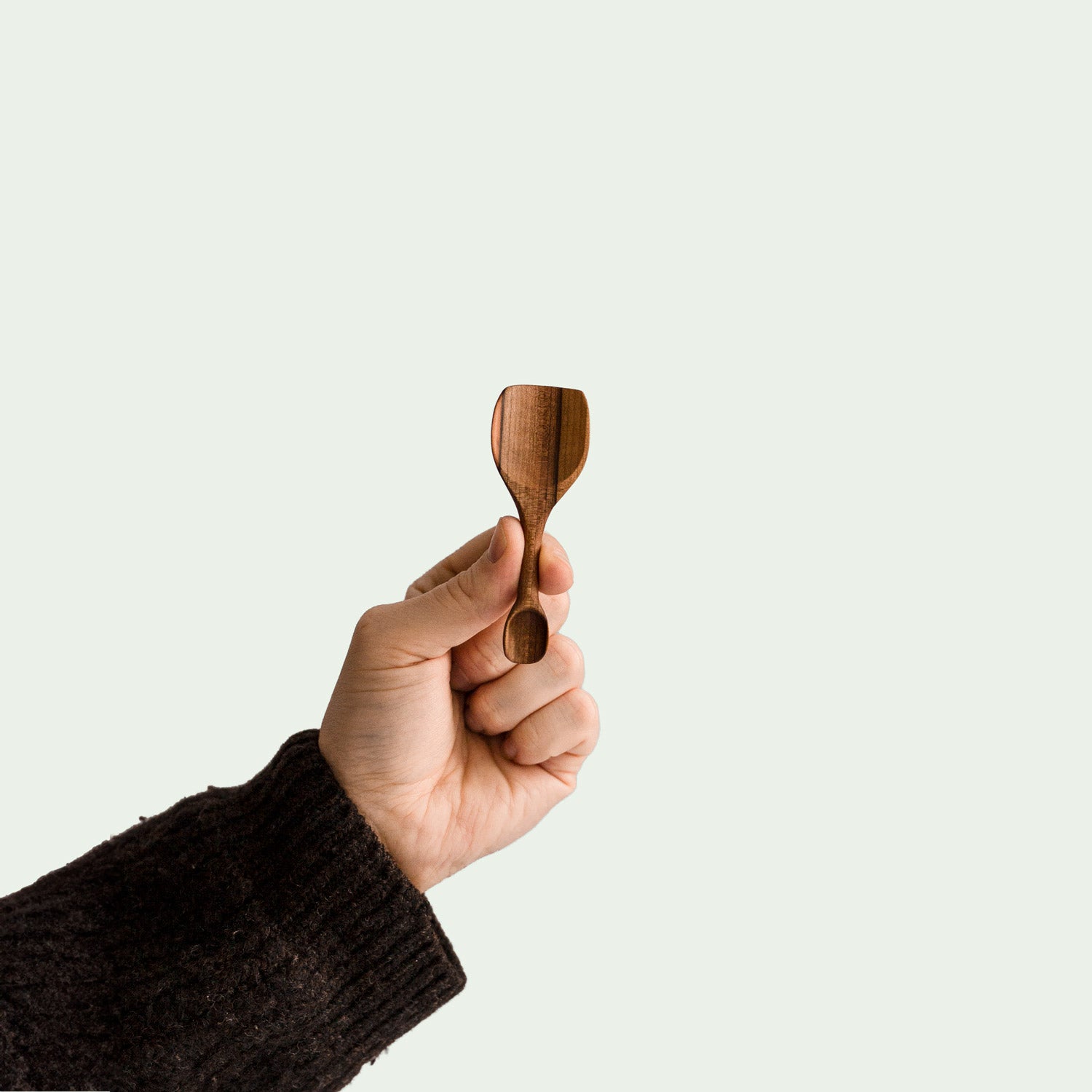 Hand hält handgefertigte doppelseitige Salzschaufel aus Elsbeere mit ergonomischem Design und glatter Oberfläche, nachhaltig produziert.
