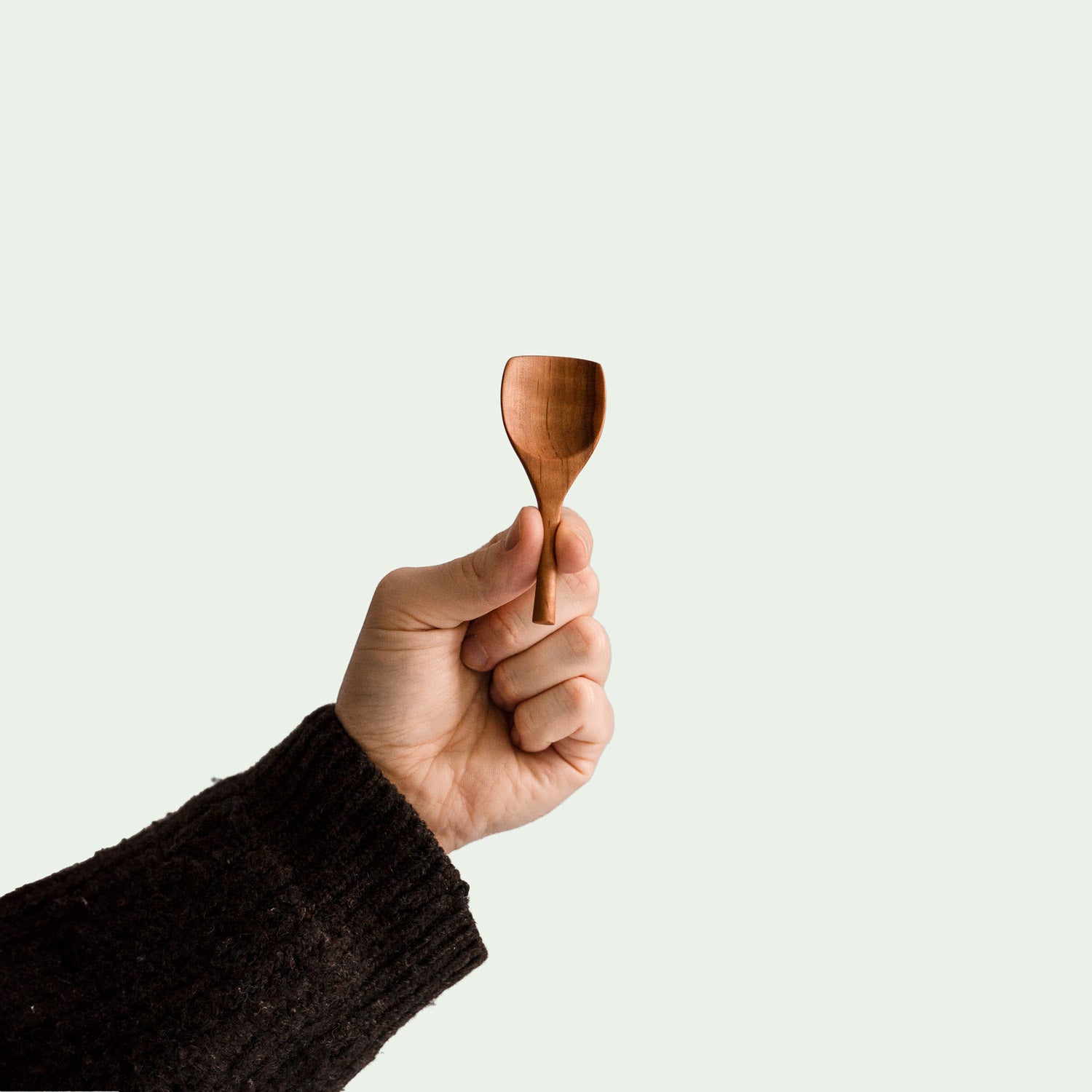 Hand hält handgefertigte Salzschaufel aus Elsbeere mit ergonomischem Design und glatter Oberfläche, nachhaltig produziert.