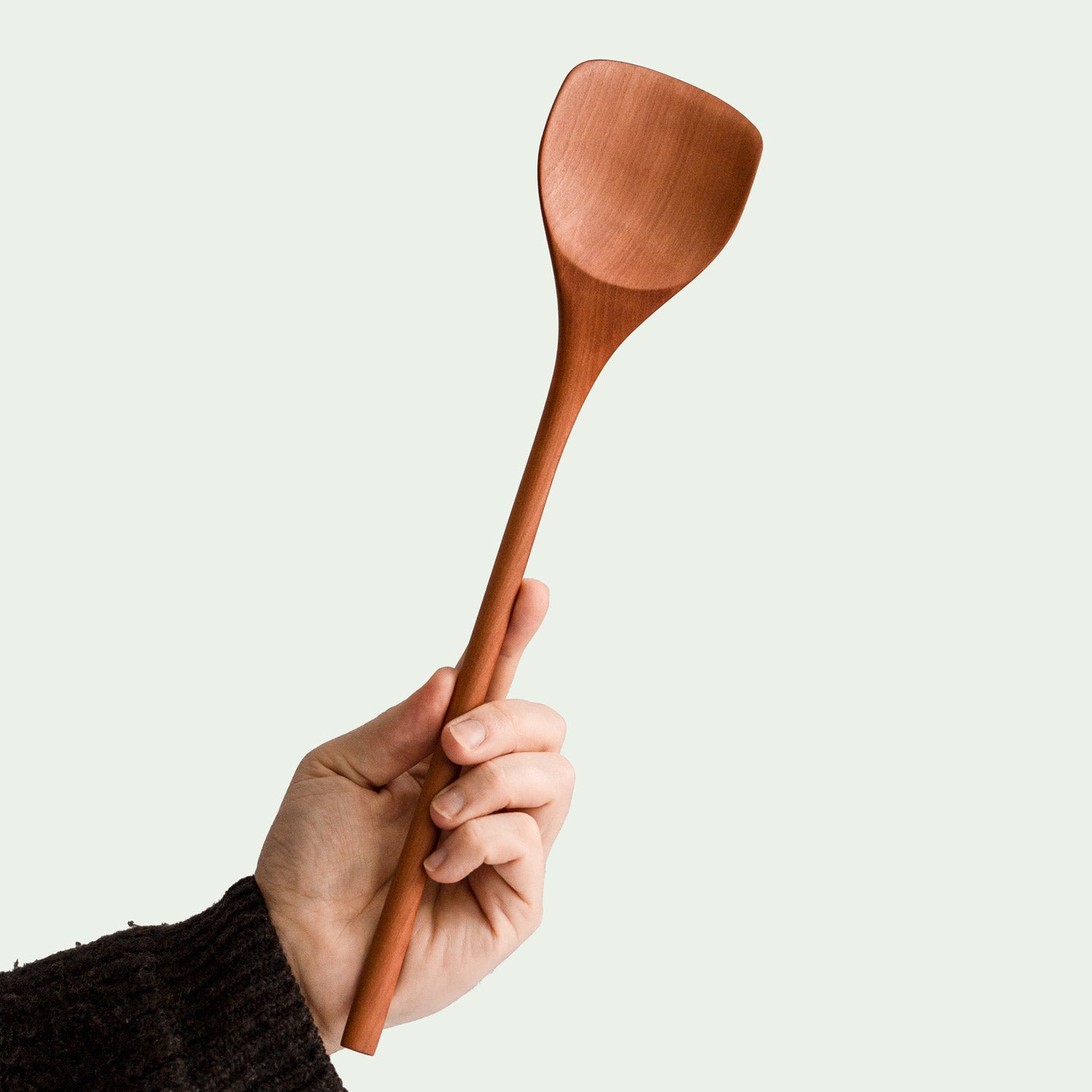 Hand hält handgefertigten Suppenlöffel aus Elsbeere mit großer, tiefen Löffelschale und ergonomischem Griff, nachhaltig produziert, diagonale Ansicht.