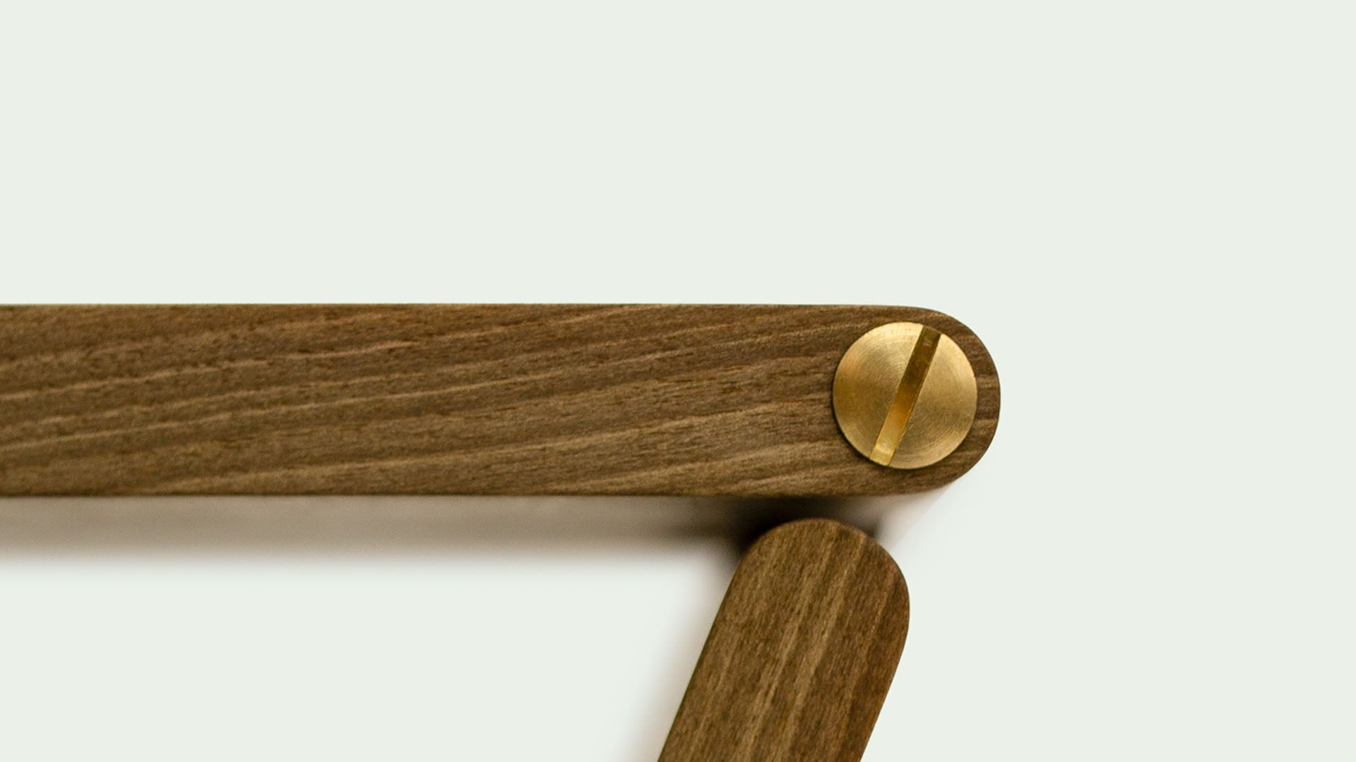 Nahaufnahme einer Holzverbindung mit einer goldenen Schraube, die zwei hölzerne Abschnitte des "Holzweg" Hockers von Marius Uminskimiteinander verbindet.