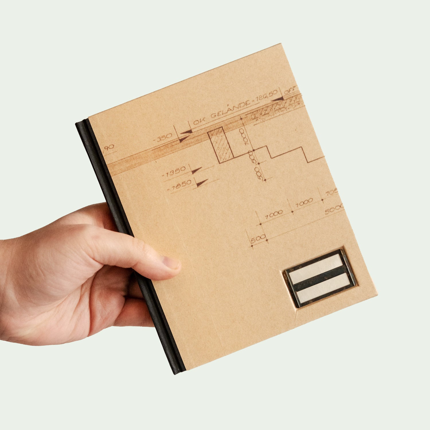 Hand hält ein Notizbuch mit technischem Zeichnungsdesign auf dem Einband.