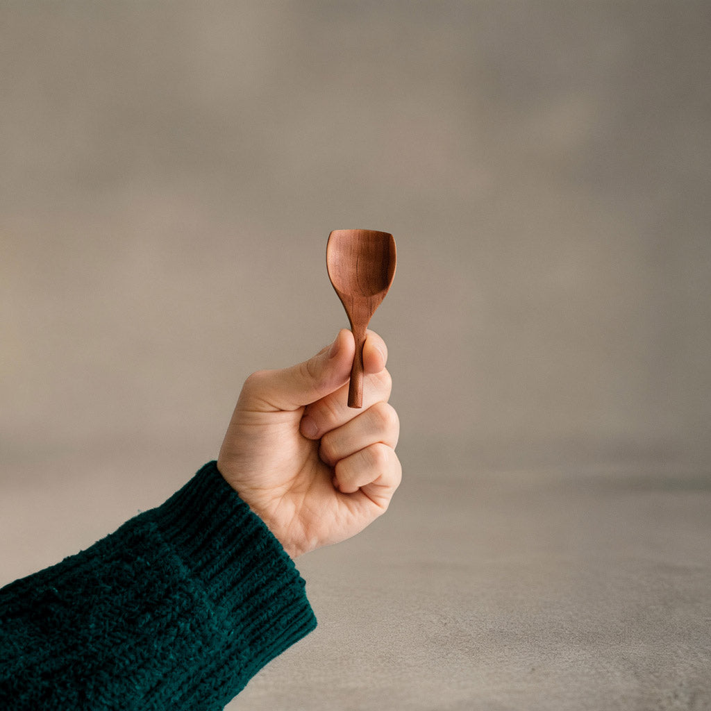 Hand hält handgefertigte Salzschaufel aus Elsbeeren Holz mit ergonomischem Design und glatter Oberfläche, nachhaltig produziert.
