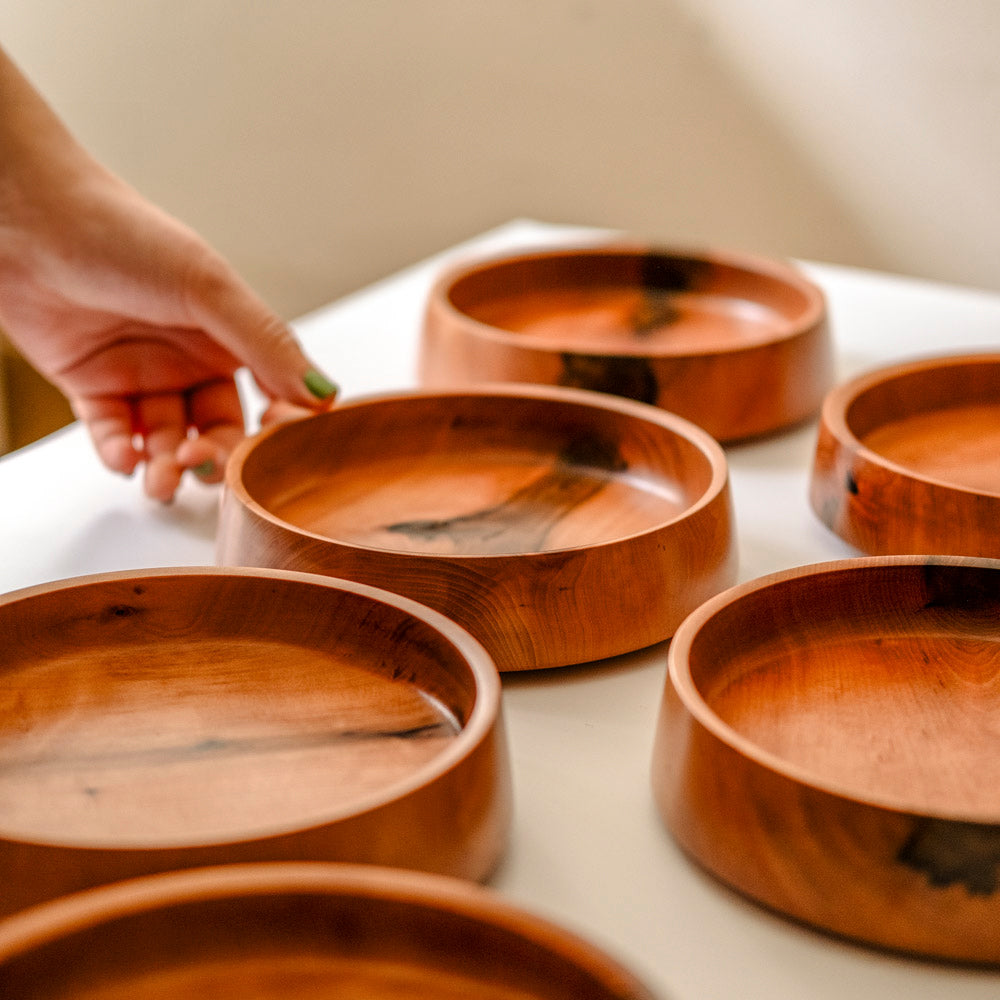 Eine Hand greift eine von vielen Kirschholz Schalen von einem Tisch