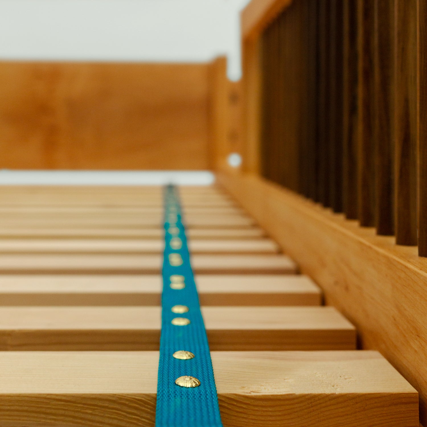 Diese Aufnahme zeigt die Lattenroste des Bettes "Liam" mit einem blauen Stoffband zur Stabilisierung. Die Seiten des Bettes sind aus Eschenholz gefertigt.