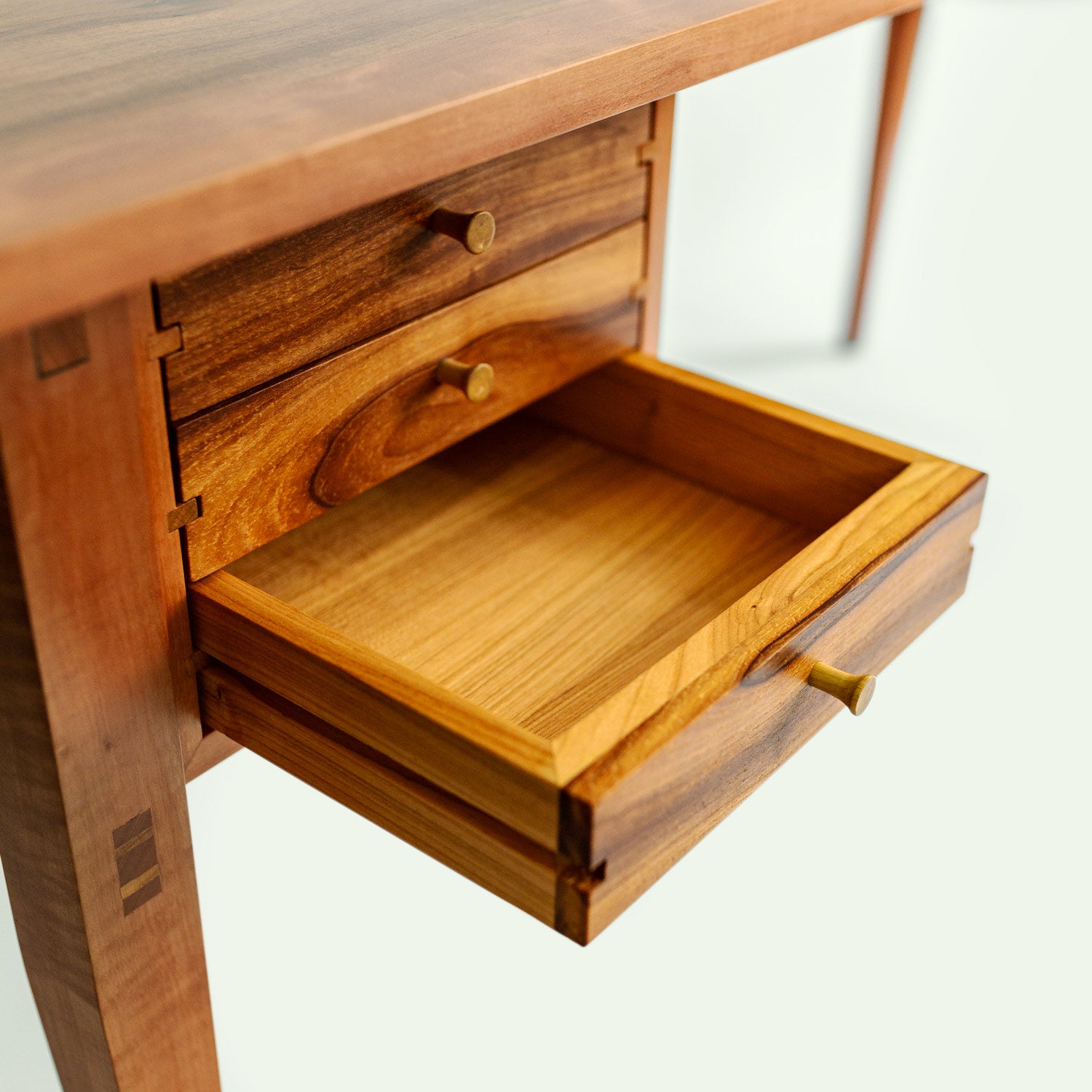 Nahaufnahme einer offenen Schublade des Holzschreibtisches "Streuobstwiese". Die Schublade zeigt die schöne Holzmaserung und die sorgfältige Handwerkskunst der Verbindungen. Die Tischplatte besteht aus Apfelholz und der Rest des Tisches aus Elsbeere.