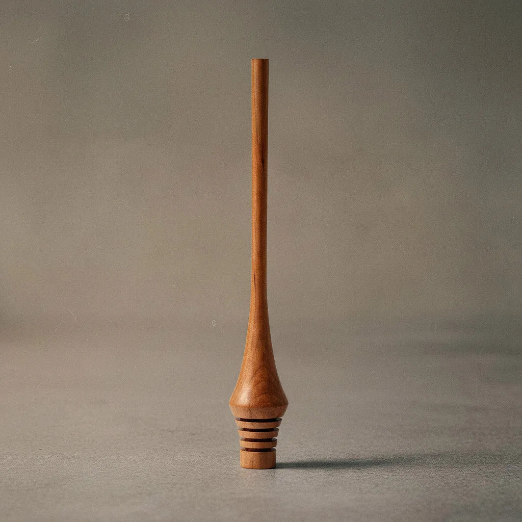 Ein Honiglöffel aus Holz, der aufrecht steht. Der Löffel hat einen langen, schlanken Griff und am unteren Ende befinden sich mehrere Einkerbungen für das Aufnehmen von Honig. Die Oberfläche des Löffels ist glatt und poliert. Handgemachter Honigheber aus Elsbeere