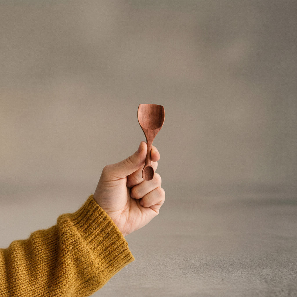 Hand hält handgefertigte doppelseitige Salzschaufel aus Elsbeere mit ergonomischem Design und glatter Oberfläche, nachhaltig produziert.