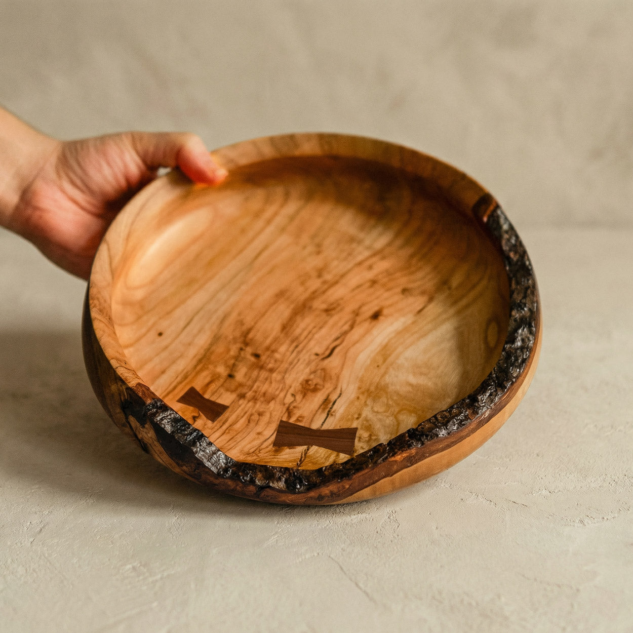 Hand hält eine handgefertigte Holzschale aus Kirschholz mit rustikalem Holzrand und einzigartiger Holzstruktur.