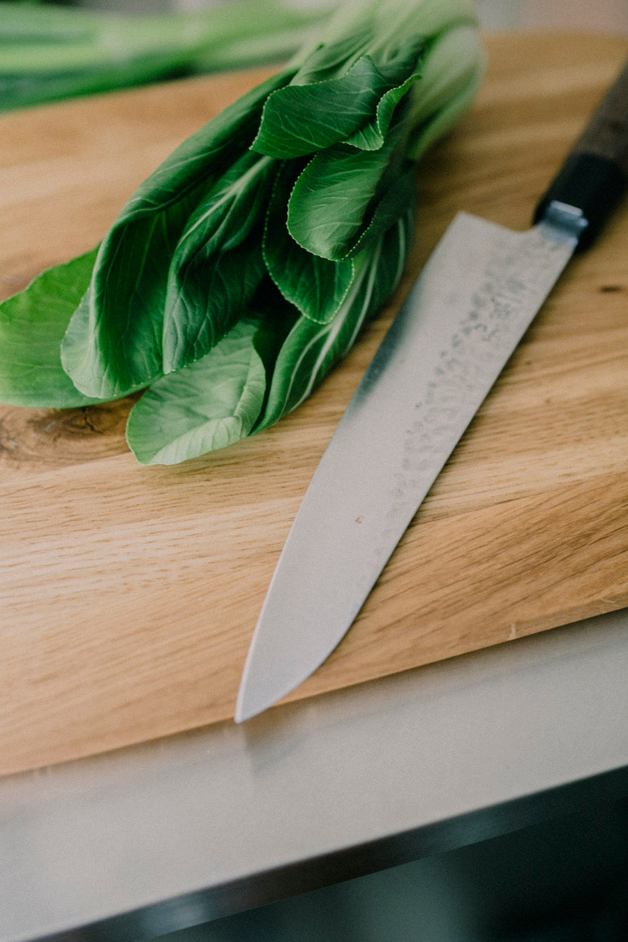 Detailaufnahme eines goßen Holz Schneidebrettes aus Eiche auf dem ein japanisches Messer und frischer Kohlrabi liegt